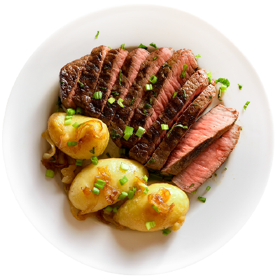 A white plate with sliced medium-rare steak, golden roasted potatoes, caramelized onions, and chopped green onions sprinkled on top.